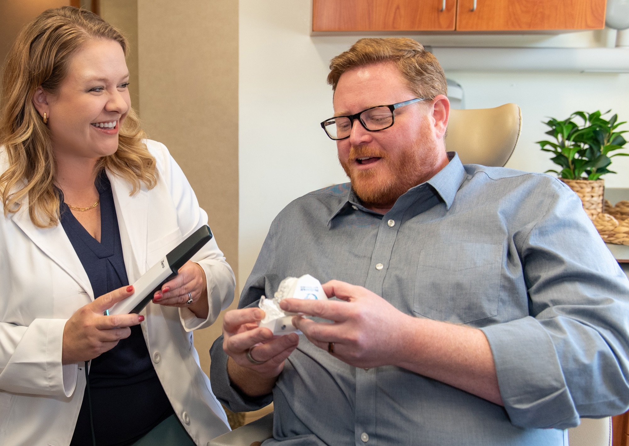 Dr. Julia Lokitis holding a digital scanner wand while a patient examines a model of his own teeth