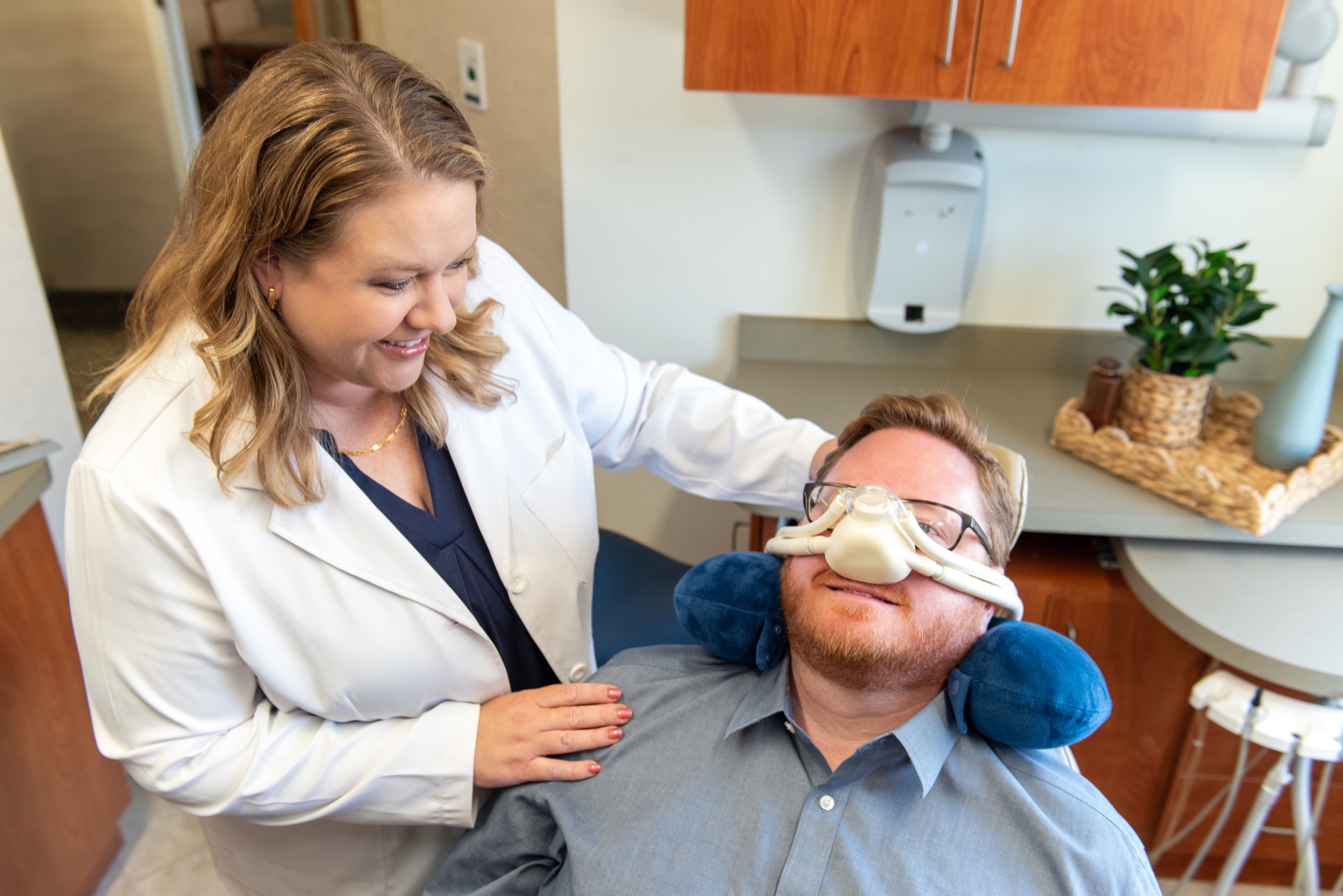 A patient wearing a nitrous oxide nasal hood with a neck pillow while Dr. Julia Lokitis rests a hand on his shoulder