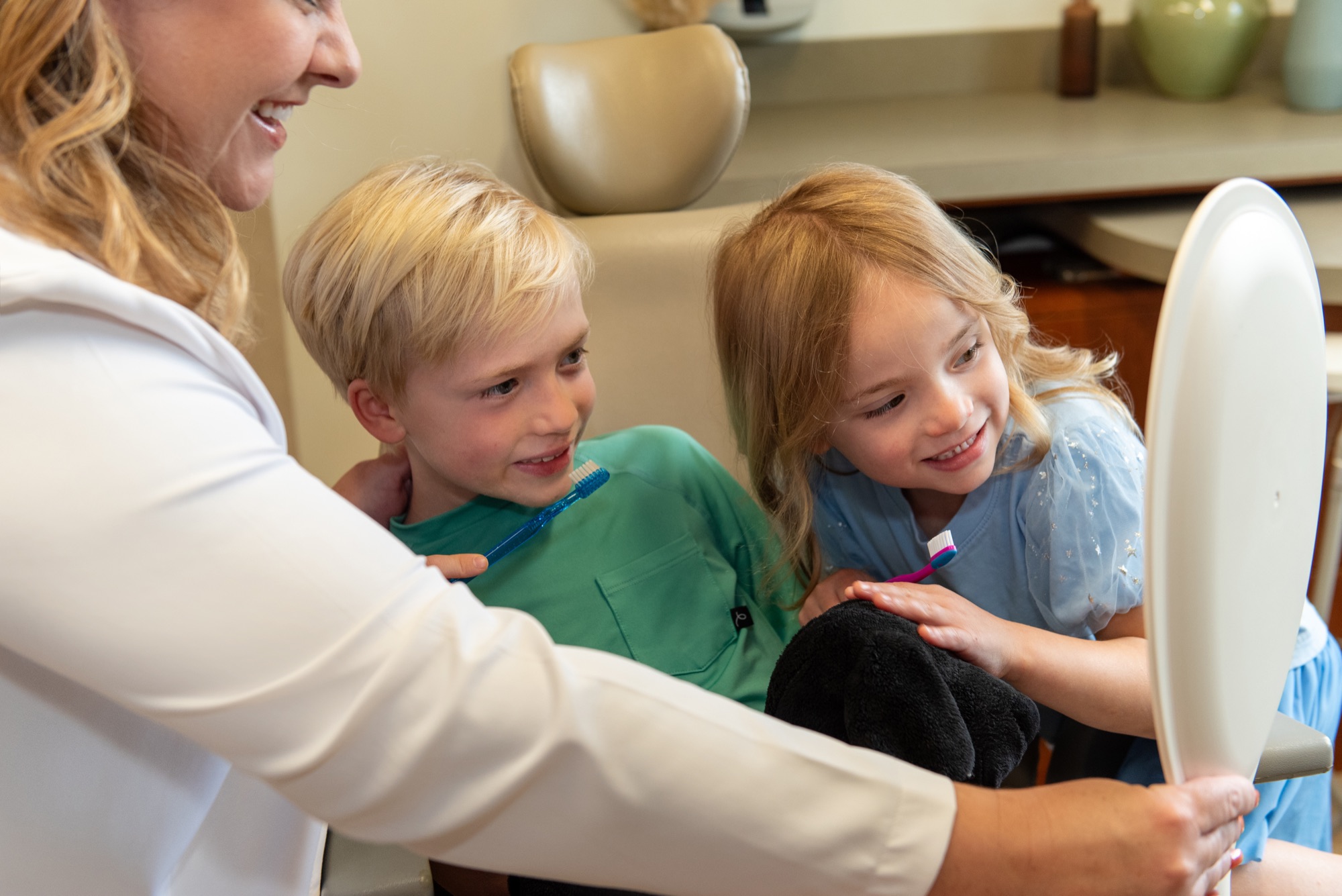 Dr. Julia Lokitis holding a mirror for two young children with toothbrushes in the treatment room
