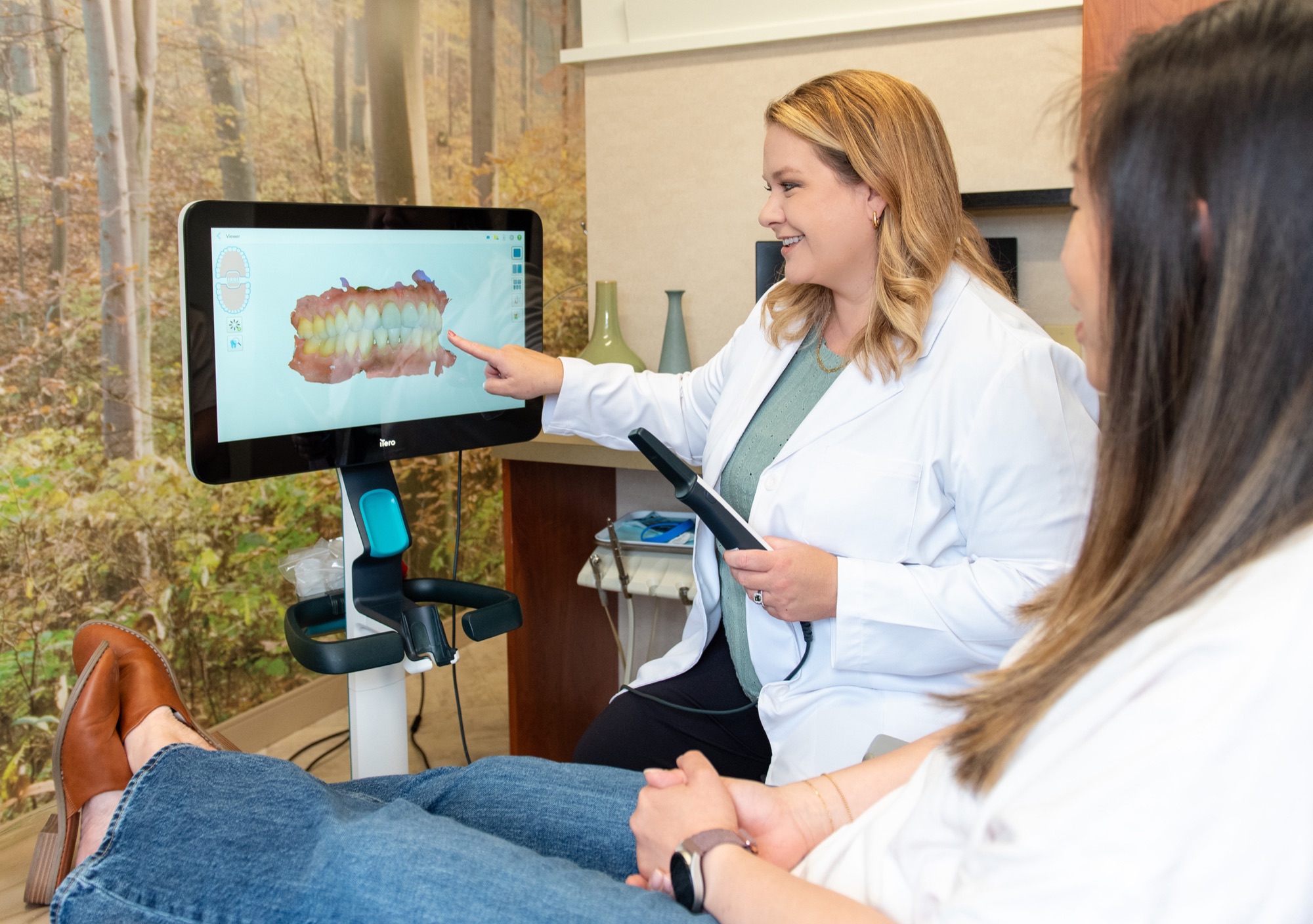 Dr. Julia Lokitis pointing out a detail on a 3D intraoral scan displayed on a large screen while a patient watches
