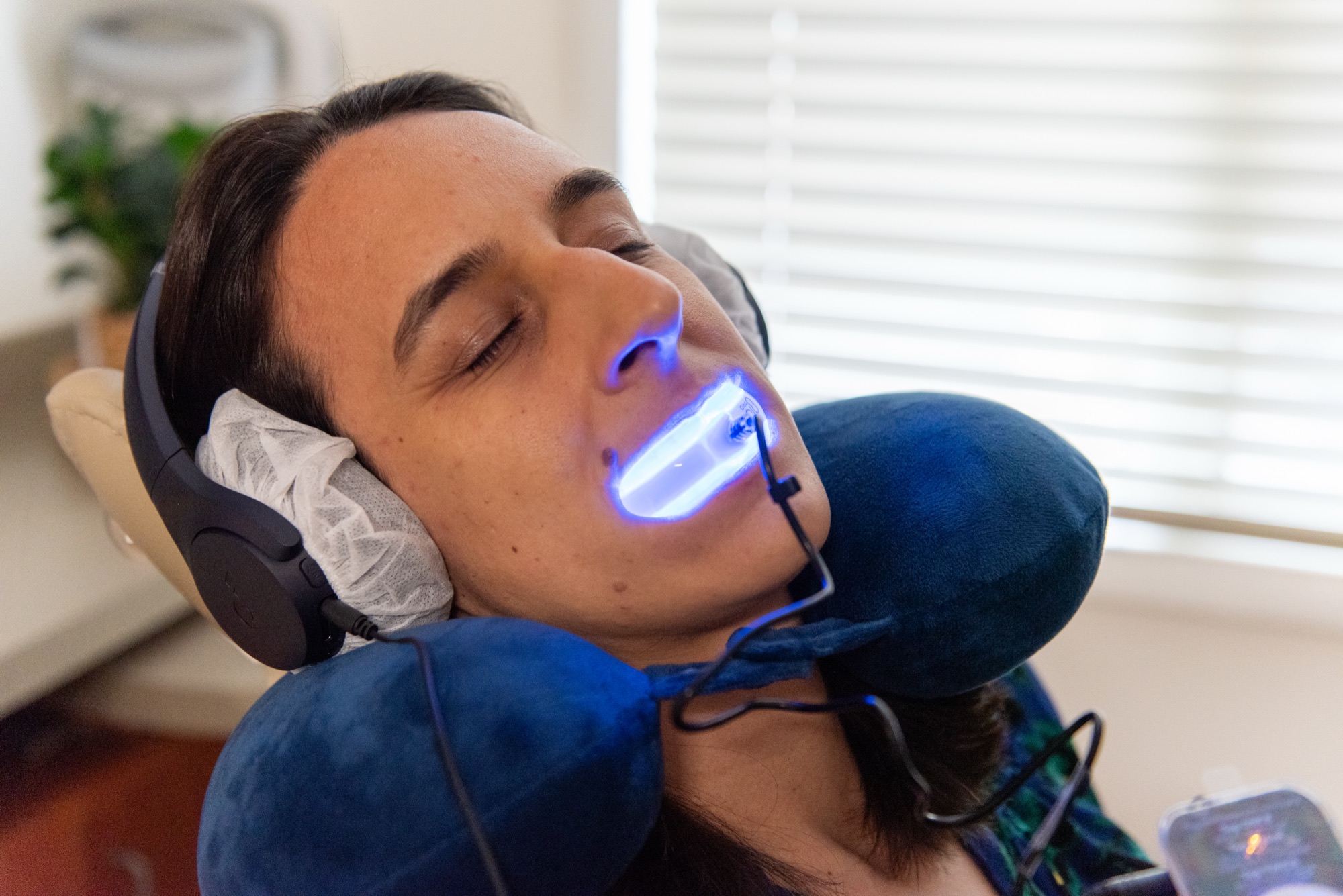A patient reclined with a neck pillow and noise-cancelling headphones during a light-activated whitening treatment at Northern Virginia Dental Solutions in Vienna, Virginia