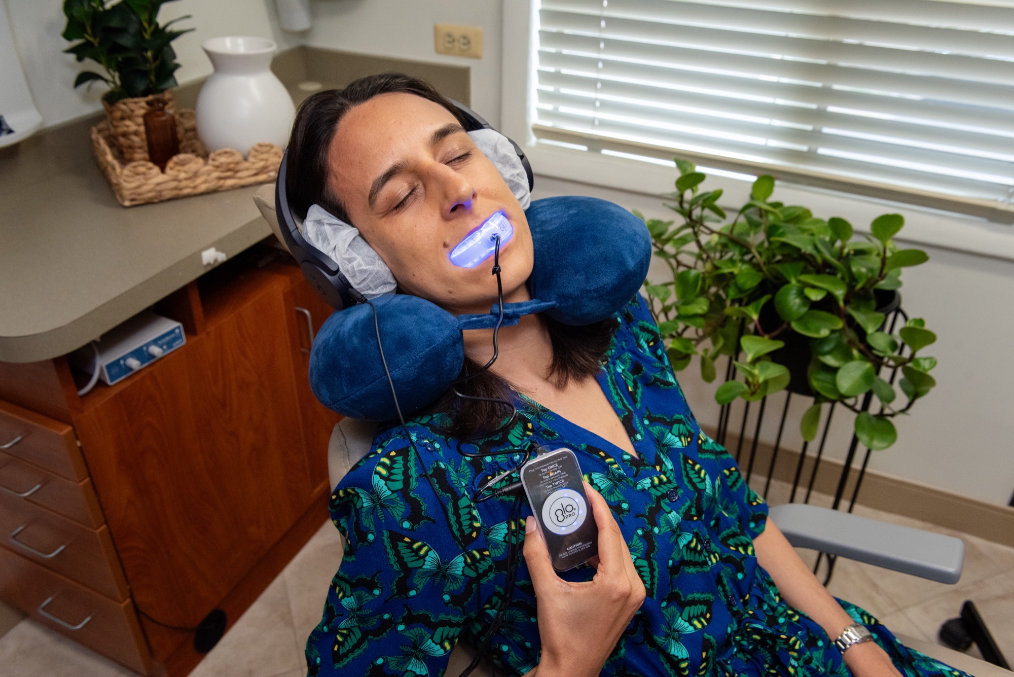 A patient using a light-activated whitening system in a treatment room at Northern Virginia Dental Solutions, resting on a neck pillow with headphones on