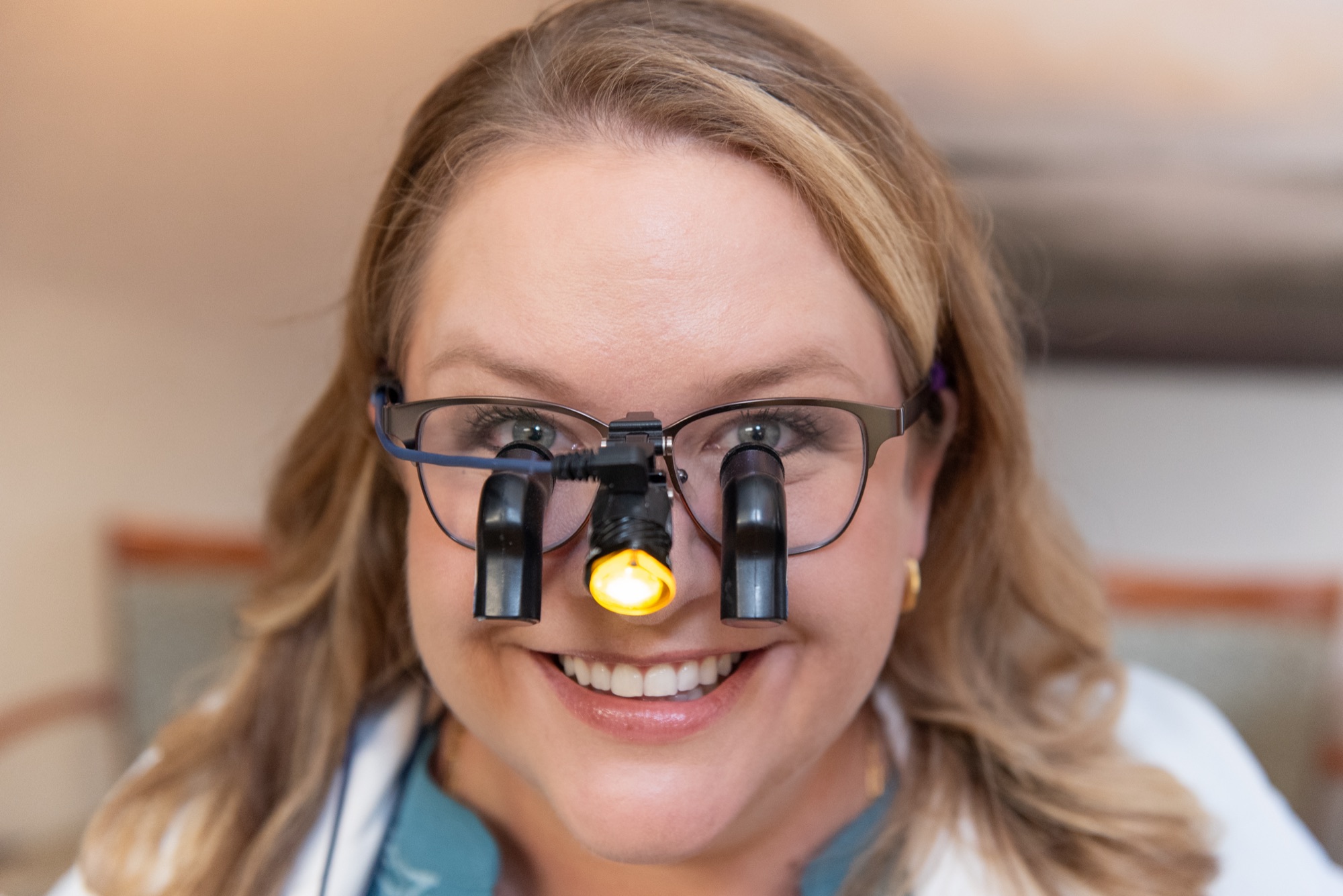 Dr. Julia Lokitis wearing magnifying dental loupes with the headlight switched on, smiling in a treatment room
