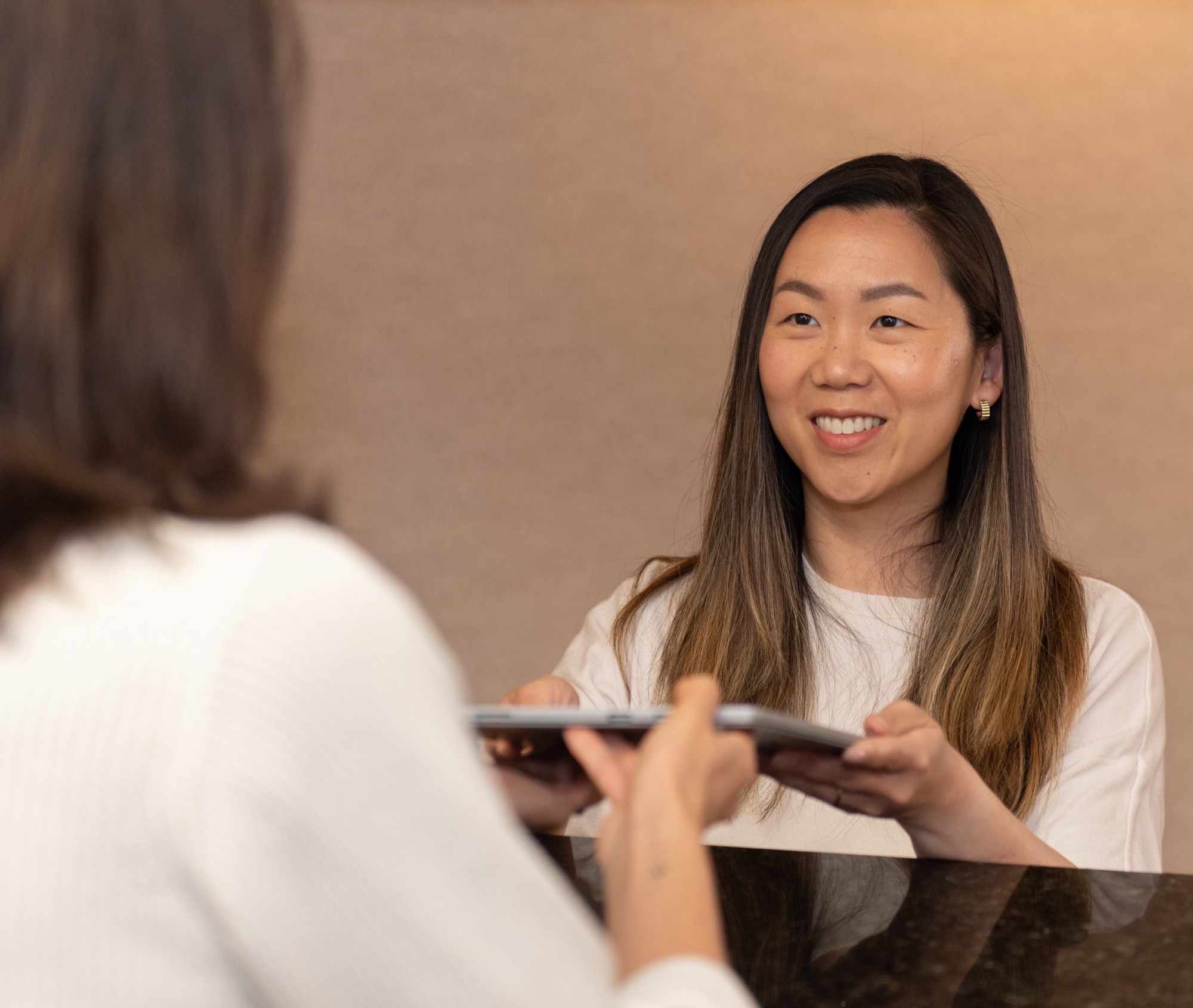 A member of the Northern Virginia Dental Solutions team at the front desk, handing a clipboard across the counter to a patient