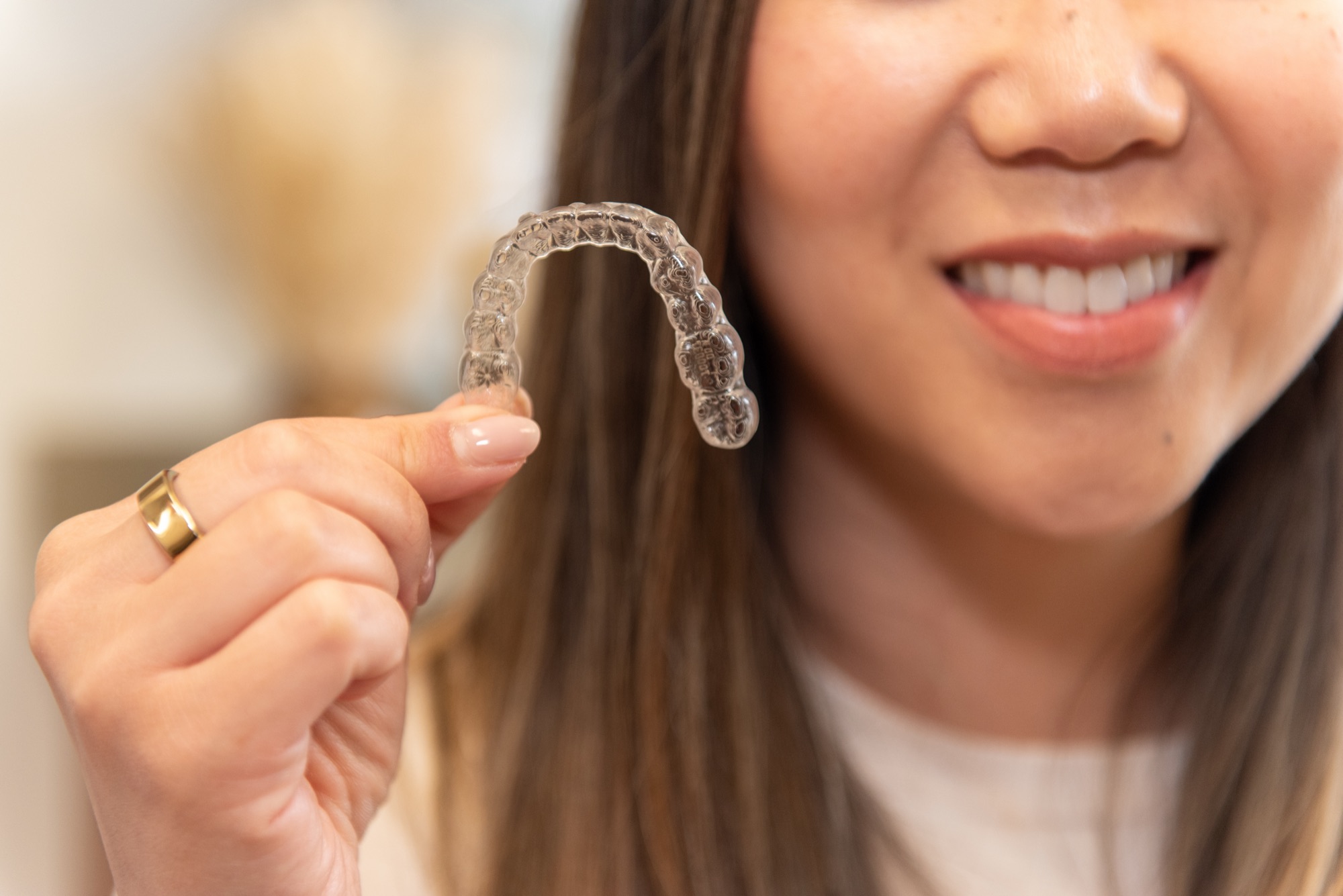 A patient holding up a clear aligner tray between her fingers, smiling