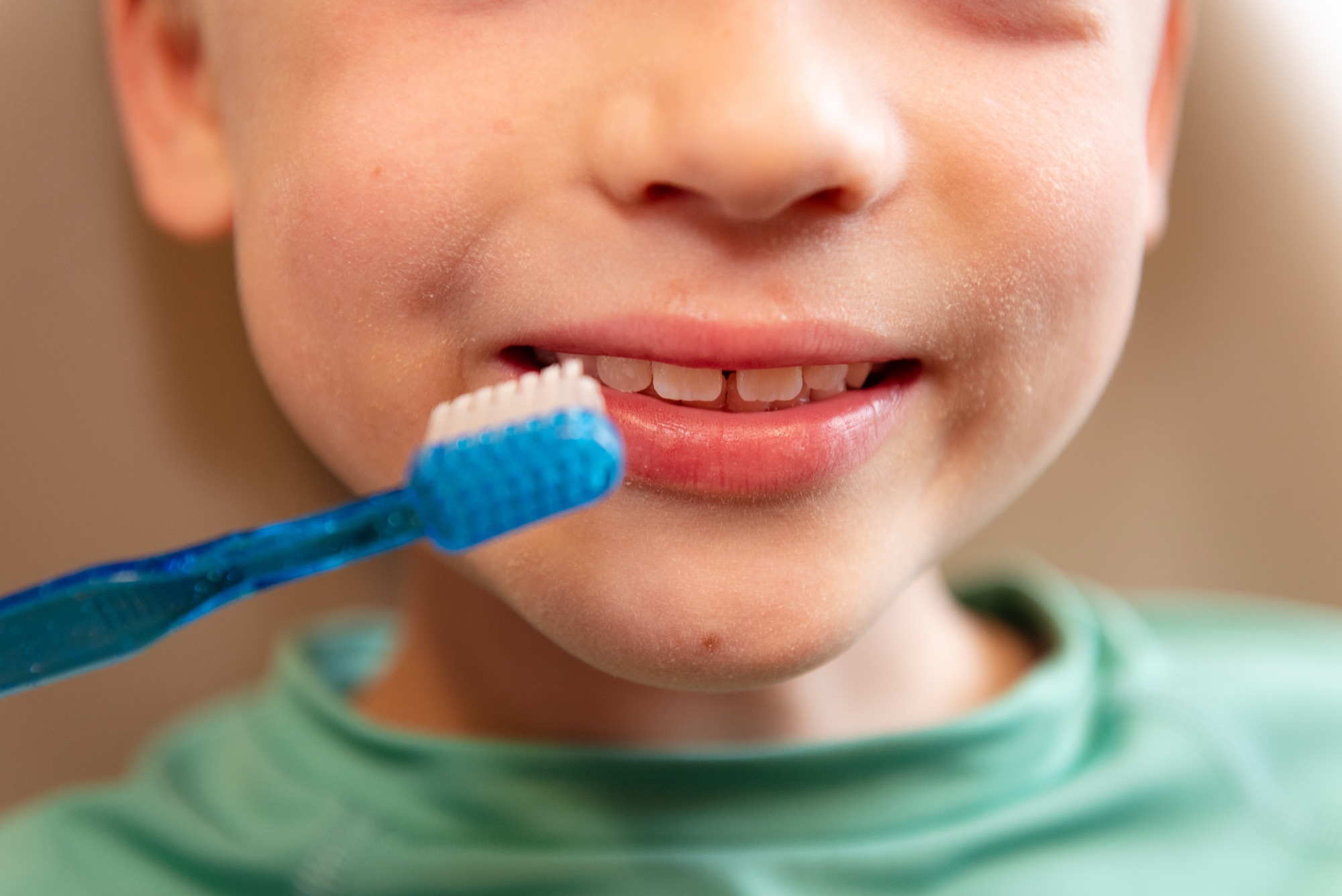 A young boy with a gap-toothed smile holding a blue toothbrush up to his teeth