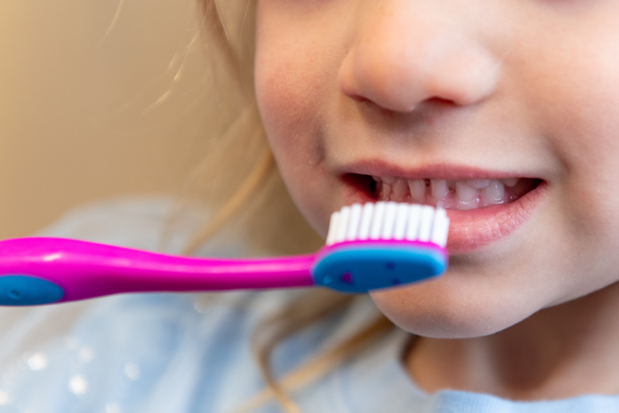 A young girl holding a pink and blue toothbrush up to her front teeth